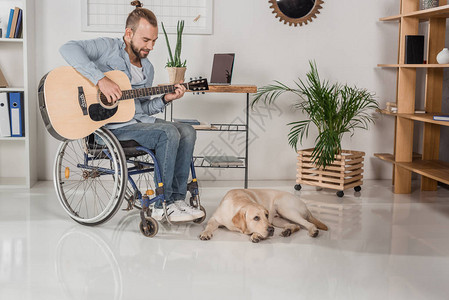 快乐的年轻残疾男子坐在轮椅上弹吉他图片
