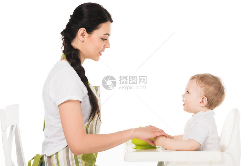 母亲用高椅子握着婴儿男孩的手在白色背图片