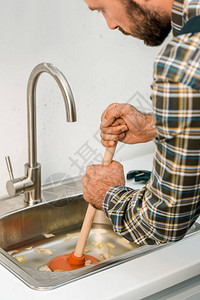 在厨房使用柱塞和清洁水槽的大胡子水管工图片