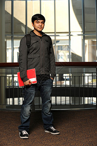 青年少数民族学生站着持有一本以大学建筑为背景的书图片