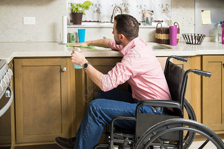 坐在轮椅上的年轻残疾男子在厨房打扫清洁图片
