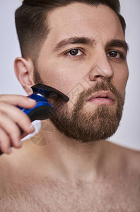年轻英俊的男人用灰色背景的电动剃须刀剃须图片
