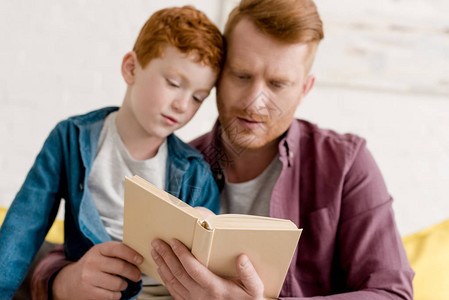 在家阅读书的专注父亲和儿子的近视图片