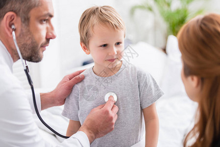 用听诊器检查生病男孩的白大衣上的儿科医图片