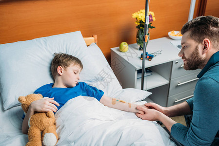 坐在生病的儿子身边躺在医院床的投放柜台图片