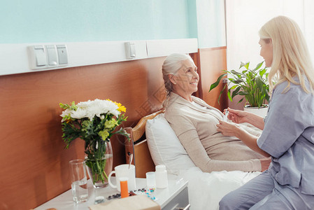 护士测量躺在医院床上微笑的老年妇图片