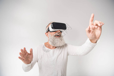高级兴奋型男子在白色上孤立的虚拟现实头盔上操纵和使用图片