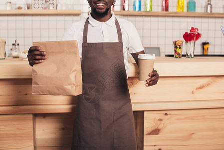 奶粉包装素材AfricanAmericanBarista在酒吧柜台持可支配咖啡杯和奶粉包背景