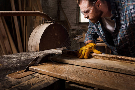 在锯木厂使用机锯拍摄的大胡子木匠戴着防图片