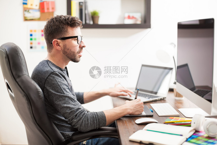 一个好看的西班牙裔年轻人在工作中同时使用两台电脑同时处理多项任务的图片
