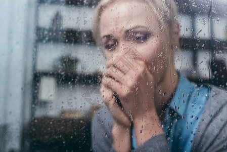 在家中通过窗户和雨滴折叠双手的成年妇女图片