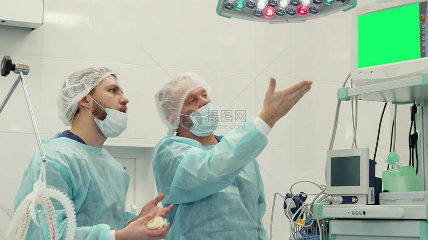 成熟的外科医生用绿色度键把他的手放在显示器上高级医生在屏幕上向他年轻的留着胡子的同事展示一些东西白种人医学专家同图片