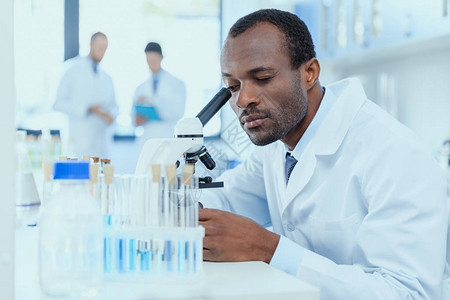 身穿白大褂的非洲裔美国科学家在实验室用显微镜工作图片