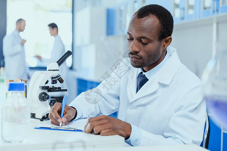 身穿白大褂的非洲裔美国科学家在实验室工作时记笔图片