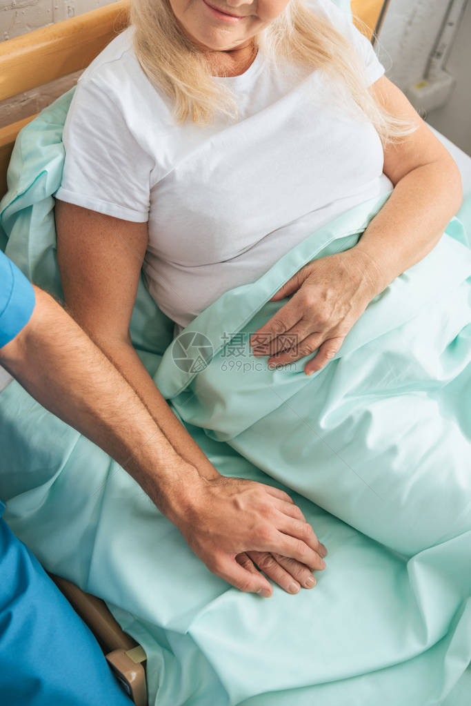 男护士与躺在医院床上的生病老年妇女握着手的男护图片