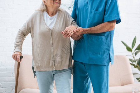 男护士用步行手杖支持高龄妇女时拍图片