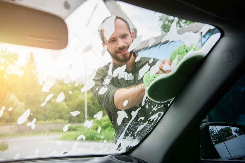 英俊的男人在洗车时用抹布和肥皂清洁汽车前窗图片