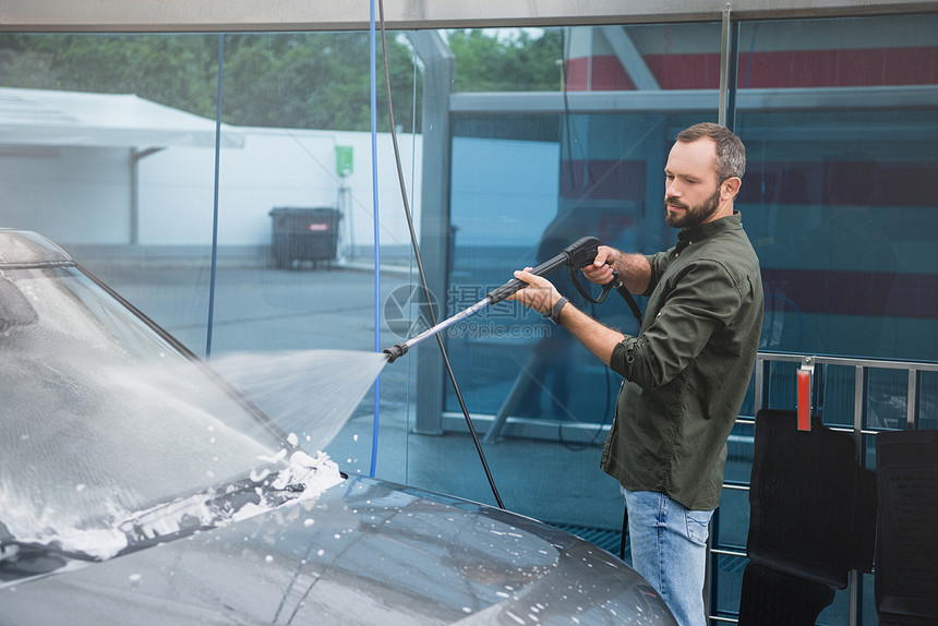 英俊的男人在用高压水射流洗车时清洁汽车前窗图片