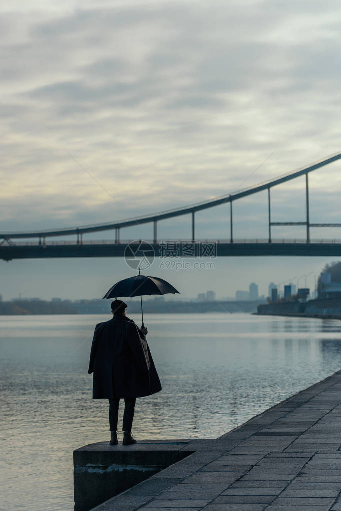 站在河岸上撑着雨伞的时髦男人图片