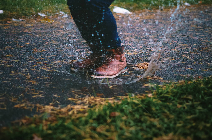 一个男孩跳进水坑溅雨水的特写镜头图片