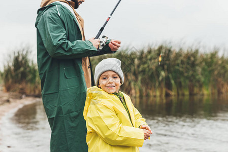 秋日快乐的儿子和父亲穿着雨衣钓鱼图片