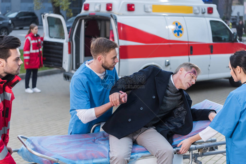 帮助伤员躺在救护车担架上的年轻医护人员图片