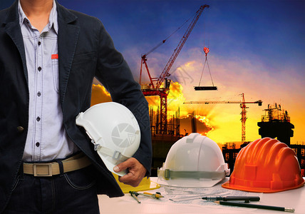有白色安全头盔的工程师男子站立在工作桌和建筑施工现场旁图片
