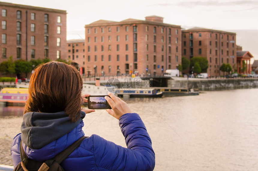 年轻女使用手机拍摄日落时在利物浦的Albert图片