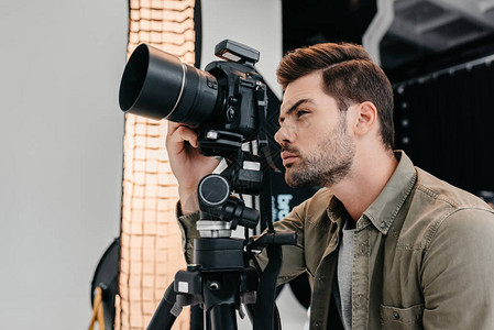 摄影工作室三脚架上带有数码摄影相机的男图片