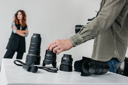 专业男摄影师在带的摄影棚中使用数码相机和镜图片