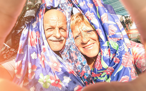 快乐的老夫妇在周游世界的服装市场自拍背景图片