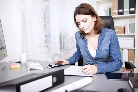 勤劳的女商人坐在办公室的办公桌前写报告图片