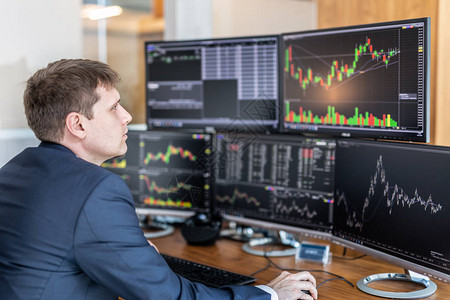 商人交易股票股票交易员在现代交易办公室的多个电脑屏幕上查看图表指数图片