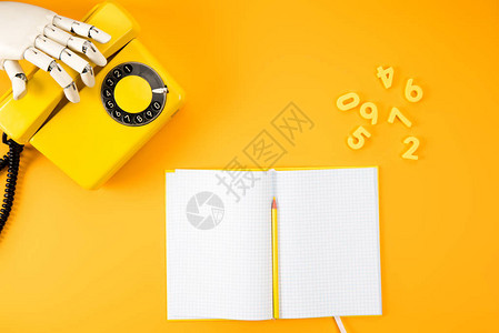 黄色桌面上用空白笔记本和数学字伸手去拿老式手机的器人图片