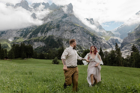 穿着婚纱的幸福新娘和新郎手牵在高山草原图片