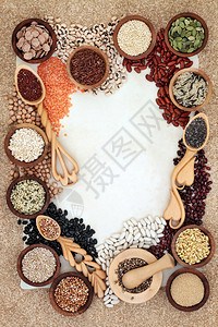 干燥的健康食品背景与豆类谷物种子和谷物在爱勺和木碗中的羊皮纸上的软木图片
