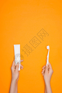 妇女持有牙刷和牙膏管以橙色背景图片