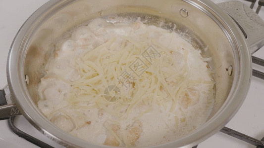 用鸡肉将奶酪添加到锅中的顶视图在平底锅里炸鸡在燃气灶上的热锅上烹饪鸡图片