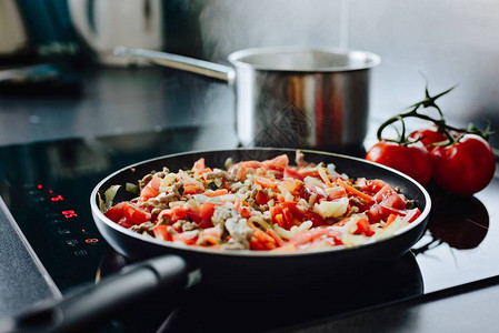 煎猪肉和橄榄油上的蔬菜在感召烹饪器上打滚锅准备意大利面背景图片