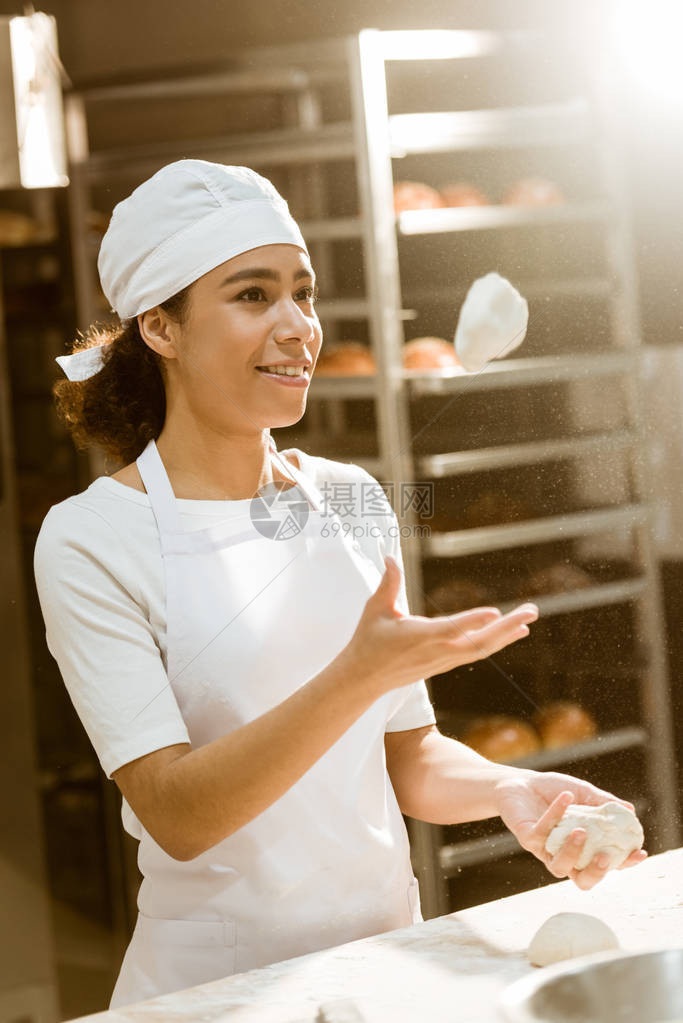 年轻的女面包师在烘焙制造厂做饭时吐生面团图片