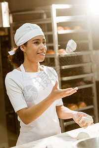 年轻的女面包师在烘焙制造厂做饭时吐生面团图片