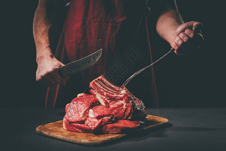 屠夫用叉子和刀在木砧板上切生肉图片