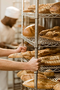 面包师拿着架子在烘烤厂配有新鲜面包图片