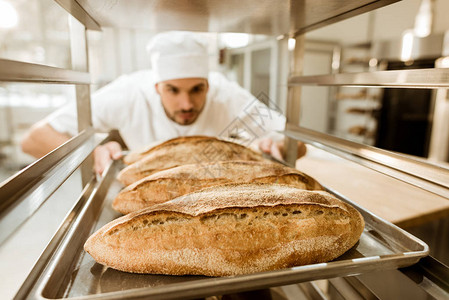 年轻面包师在烘烤生产时将新鲜面包托图片