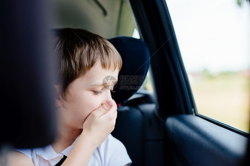 坐在儿童座椅上的汽车后座上的7岁小孩用手捂住嘴患有晕车图片