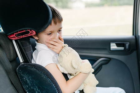 坐在儿童座椅上的汽车后座上的7岁小孩用手捂住嘴患有晕车背景