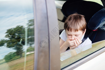 坐在儿童安全座椅上的汽车后座上的7岁小孩用手捂住嘴患有晕车图片