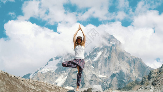 年轻女子在山上雪山背景下做瑜伽时表演亚萨那树Vriksasana图片