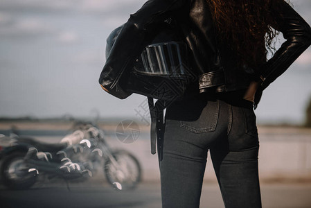 持有摩托头盔站在背景的摩托车的妇图片