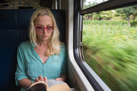 金发白种女人在火车窗边看书图片